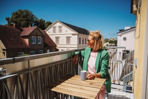 Un balcón con una mesa de madera y una taza a rayas, con vistas a una calle con edificios tradicionales.