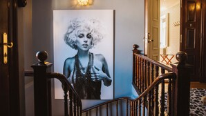 A hallway with a large framed portrait, a wooden staircase, and a door leading to another room. - Köpmans - Boutique Hotel (Hoganas)