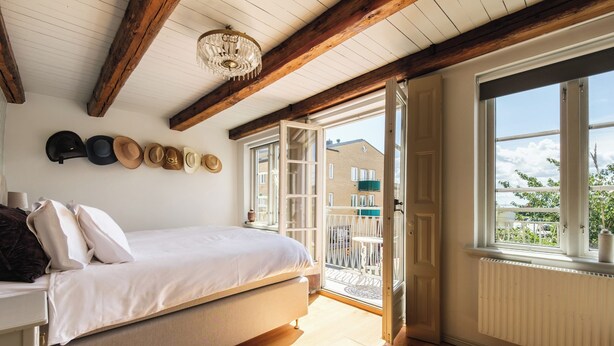 A bedroom with a bed, wooden beams, a chandelier, and a view of the outside. - Köpmans - Boutique Hotel (Hoganas)