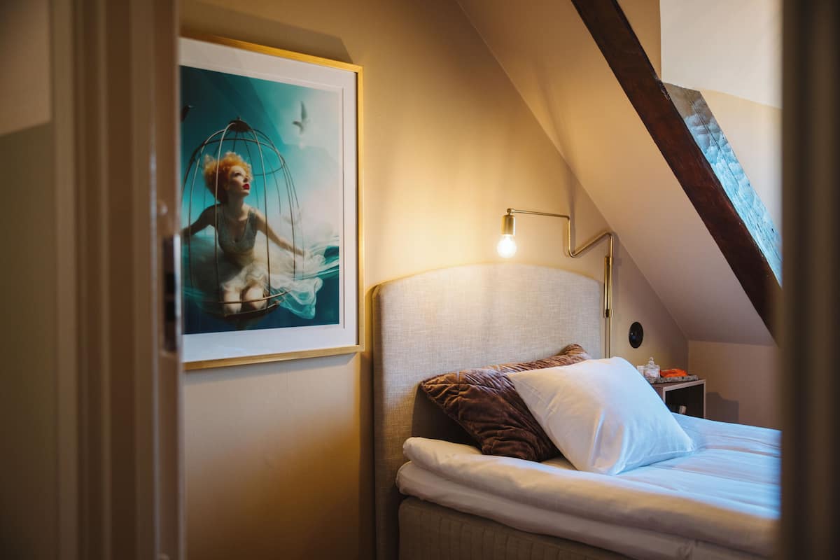 Une chambre à coucher avec un lit, une table de chevet, un tableau encadré au mur et un plafond en pente.