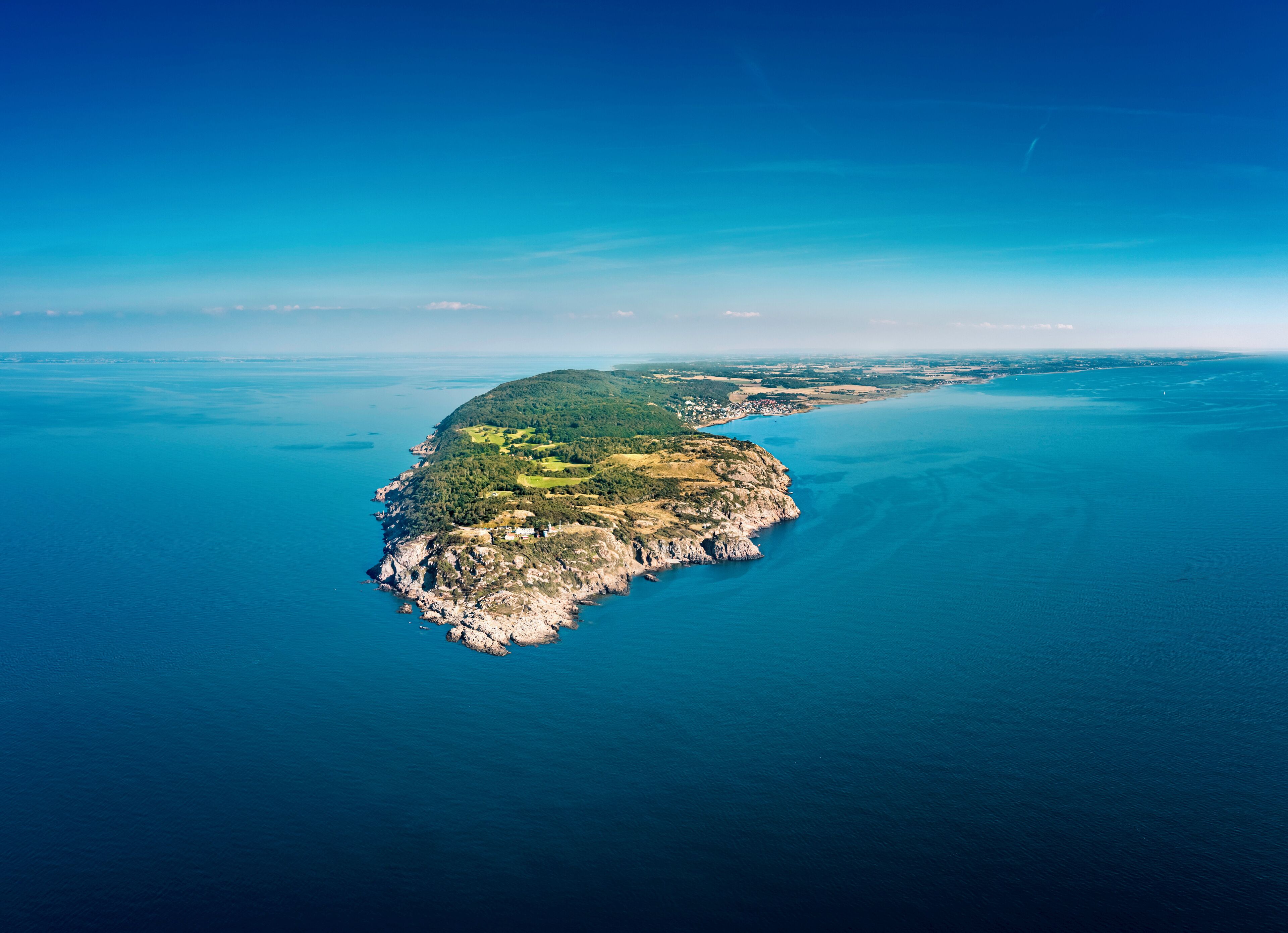 Vista aérea de una isla costera con un pequeño asentamiento, rodeada de un mar azul intenso.