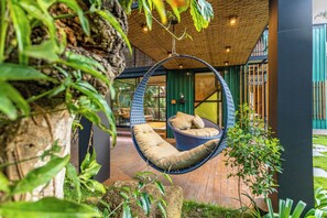 A hanging chair in a lush, green outdoor area with a wooden ceiling and a view of the interior. - Casa Natu Ilhabela  (Ilhabela)