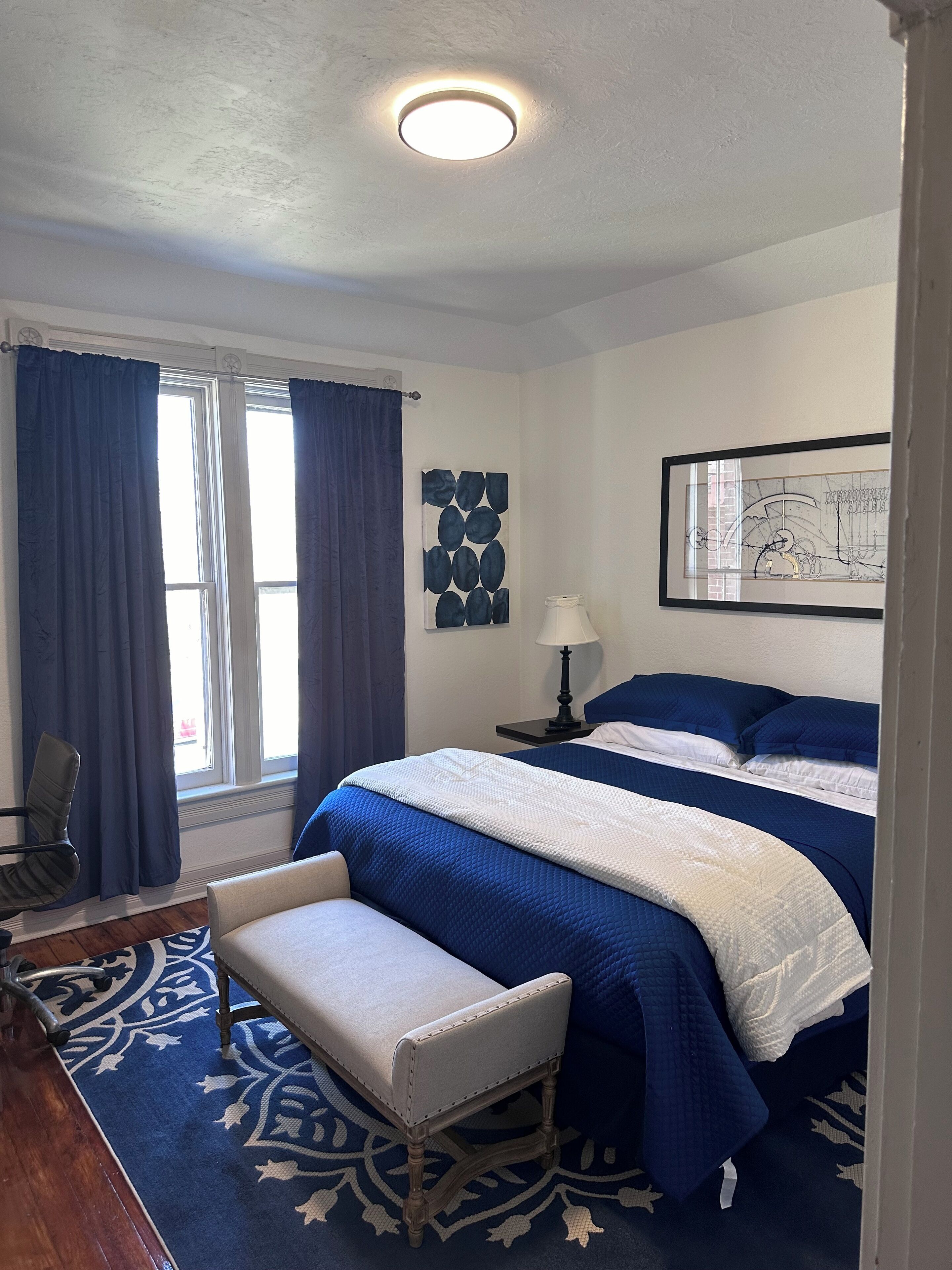 A bedroom with a large bed, a bench, a nightstand, and a window with curtains.