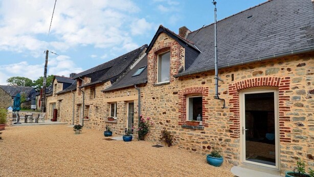 Une rangée de bâtiments en pierre donnant sur une cour en gravier, avec des espaces de repos en plein air et des plantes en pot.