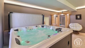 Une salle de spa équipée d’un bain à remous, d’un sauna en bois et d’un fauteuil blanc.