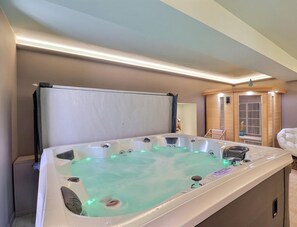 Une salle de spa équipée d’un bain à remous, d’un sauna en bois et d’un fauteuil blanc.