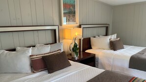 A hotel room with two beds, each with white bedding and brown accents. There is a nightstand with a lamp and a potted plant between the beds. - Loblolly Pines Adventure Camp (Eureka Springs)