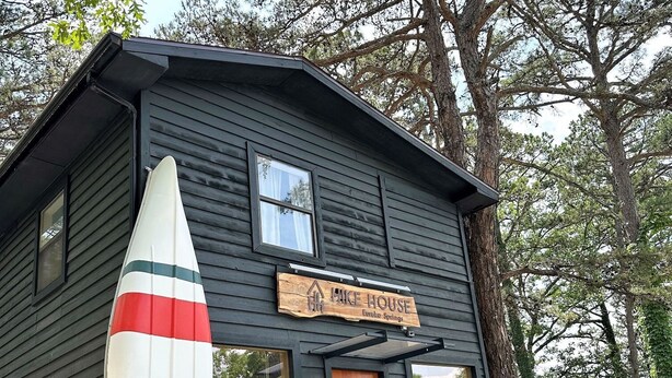 A small wooden building labeled "Hike House" with a large surfboard outside. - Loblolly Pines Adventure Camp (Eureka Springs)