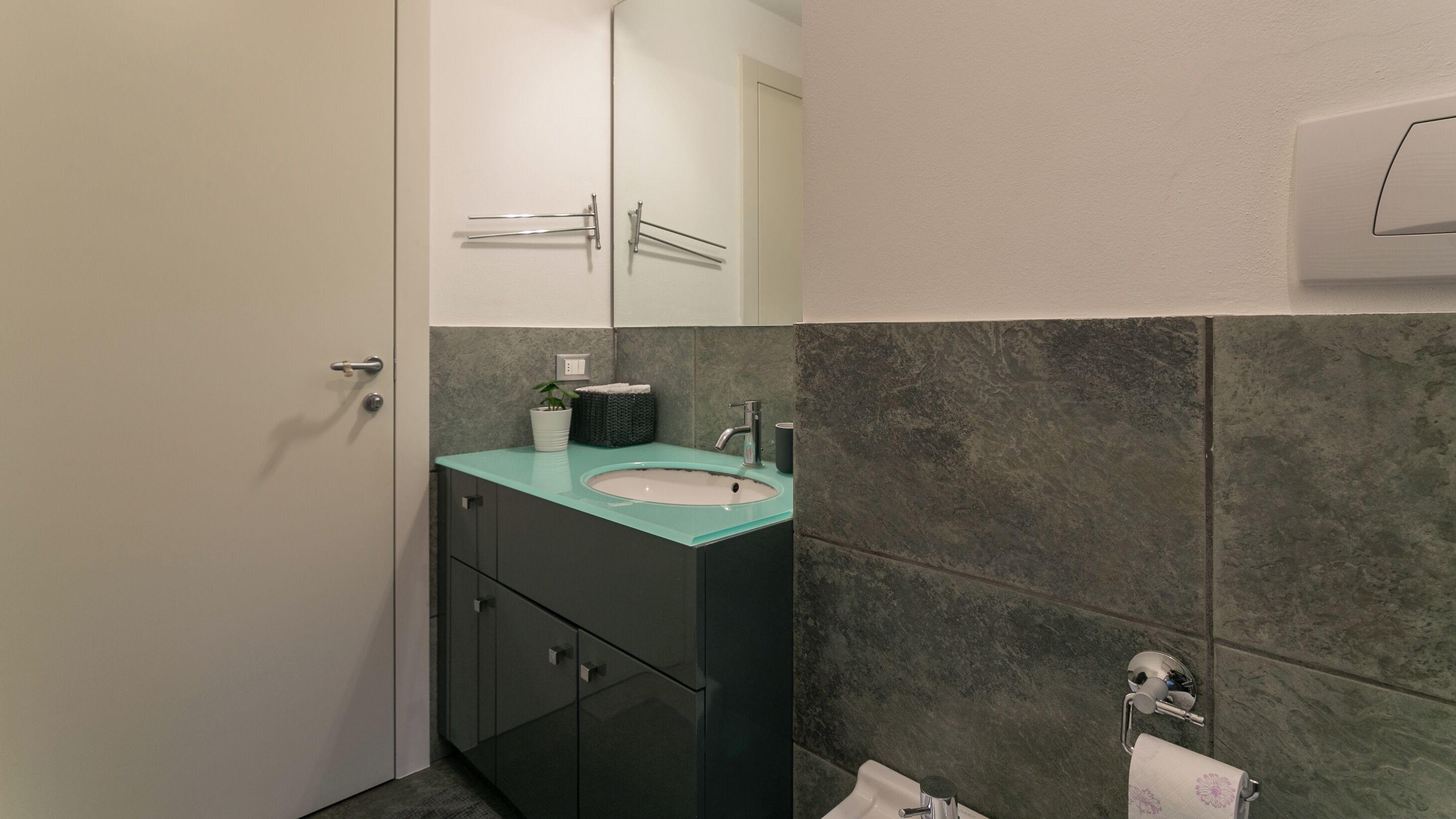 Un baño con lavamanos, espejo, armarios y un perchero para toallas.