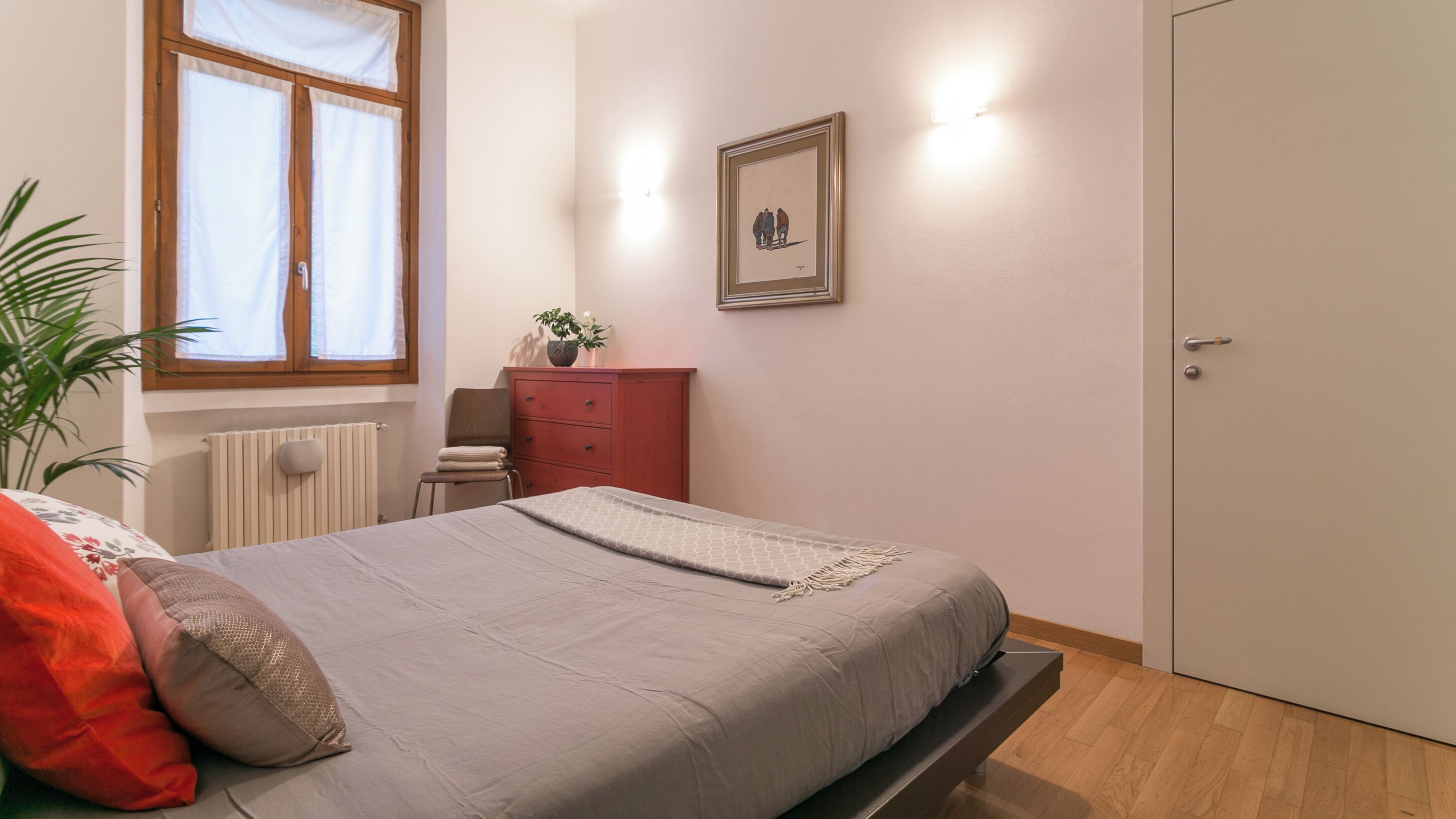 Une chambre à coucher avec un lit, une commode, un radiateur, une fenêtre et une porte.