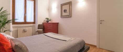 Une chambre à coucher avec un lit, une commode, un radiateur, une fenêtre et une porte.