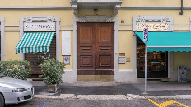 Katunäkymä, jossa näkyy suljettu liike nimeltä SALUMERIA GALLONI, pysäköintikielto-opaste ja rakennus, jossa on opaste Il Pier Lombardolle.