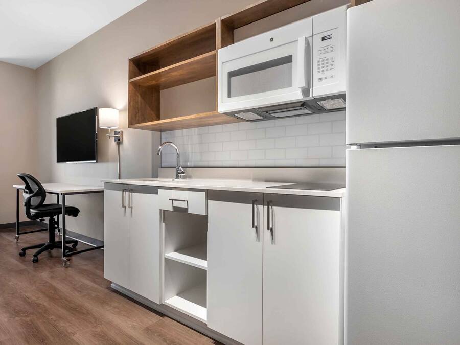 A modern kitchen with white cabinets, a microwave, a sink, and a chair.
