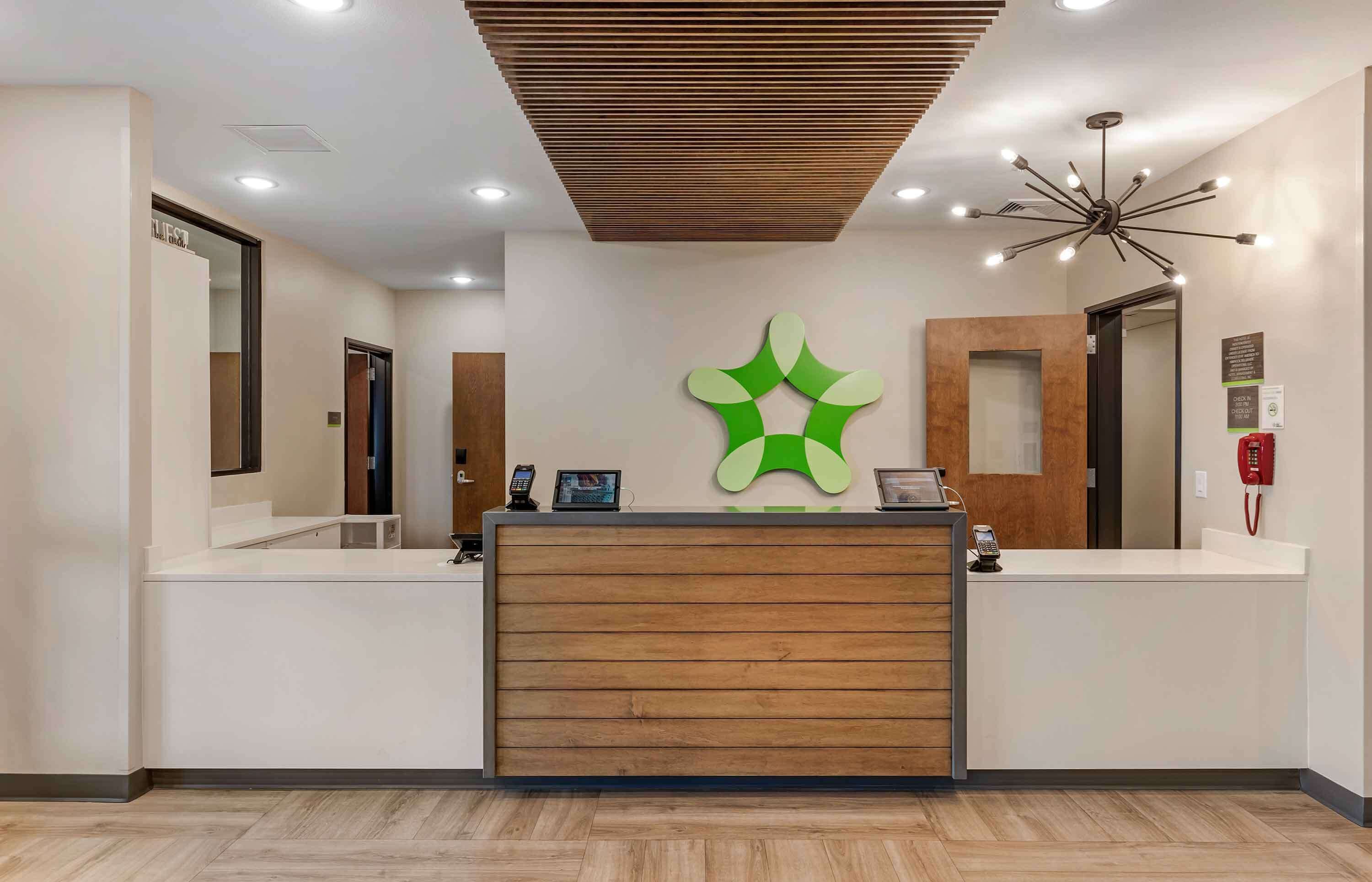 A reception desk with a wooden finish, a green logo, and a modern chandelier.