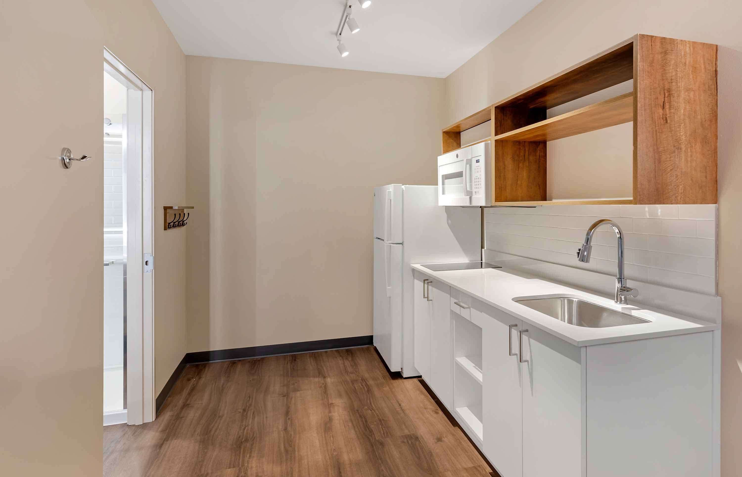A modern kitchen with white cabinetry, a stainless steel sink, and wooden shelves above the countertop.