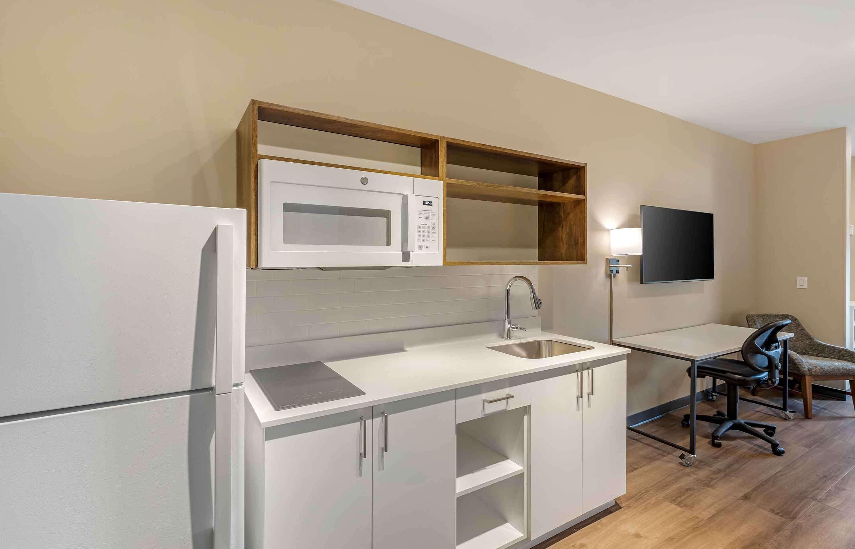 Cocina compacta con microondas, pileta y pequeño comedor con una silla.