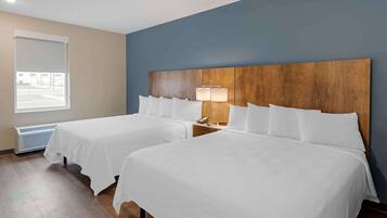 Quarto de hotel com duas camas, cabeceira de madeira, luminária e janela com vista para um estacionamento.