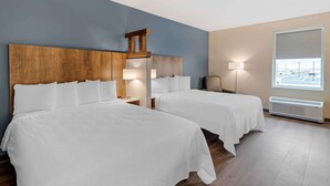 Habitación de hotel con dos camas, cabecero de madera, lámparas de noche, ventana con vistas y un calefactor.