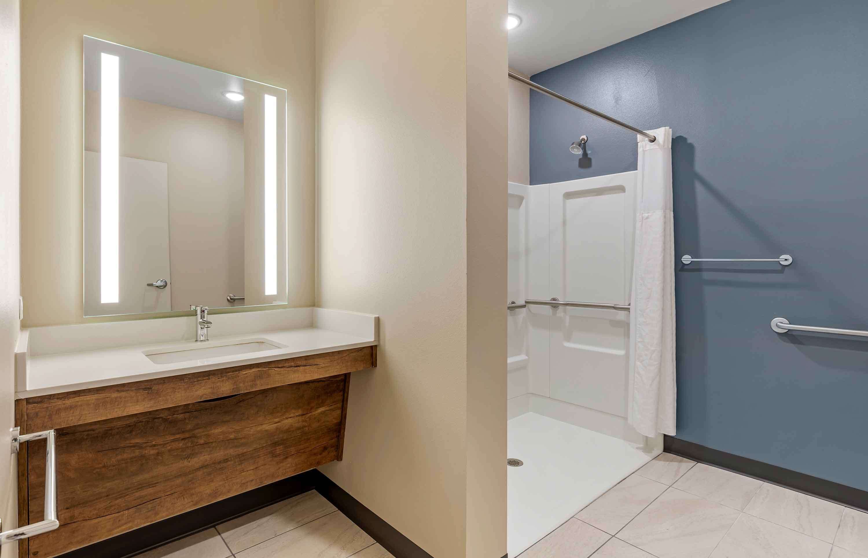 Un baño con tocador de madera, un espejo grande y una ducha con puerta de cristal.