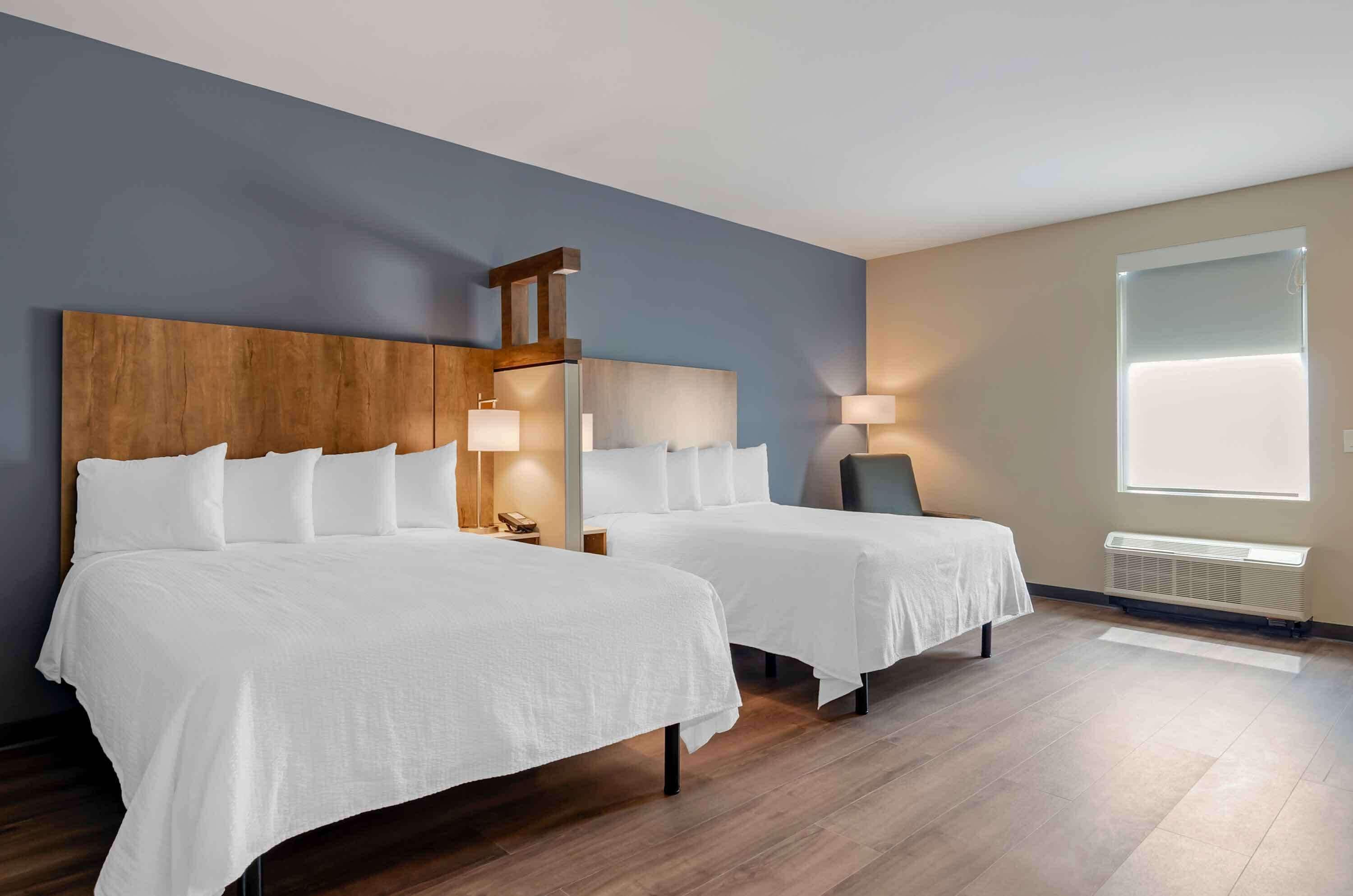 Een hotelkamer met twee bedden, een houten hoofdbord, bedlampjes, een raam met zonwering en een radiator.