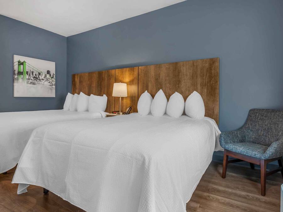A hotel room with two beds, a wooden headboard, a lamp, and a chair.