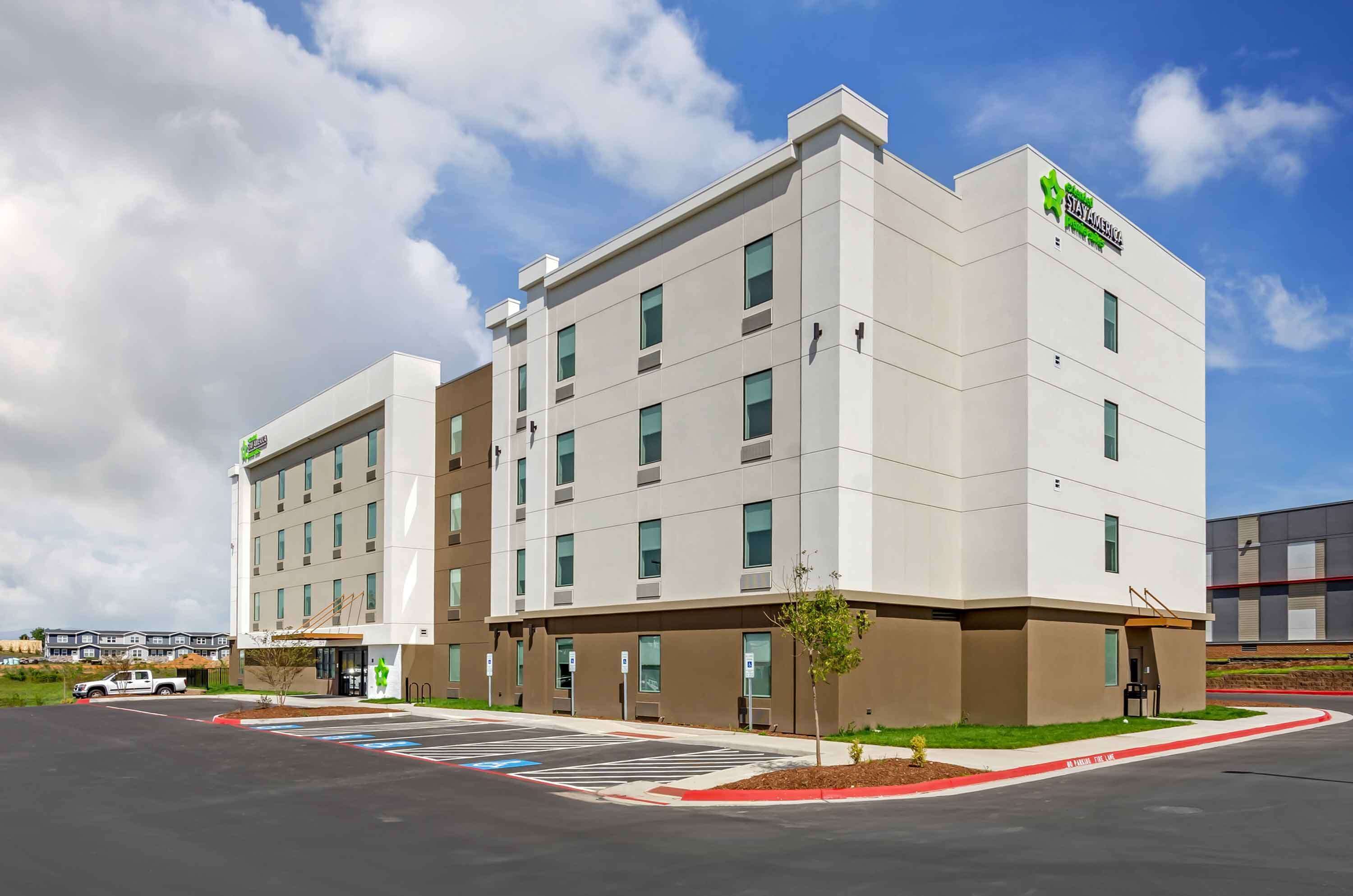 A modern hotel with a flat facade, multiple windows, and a parking lot in front.