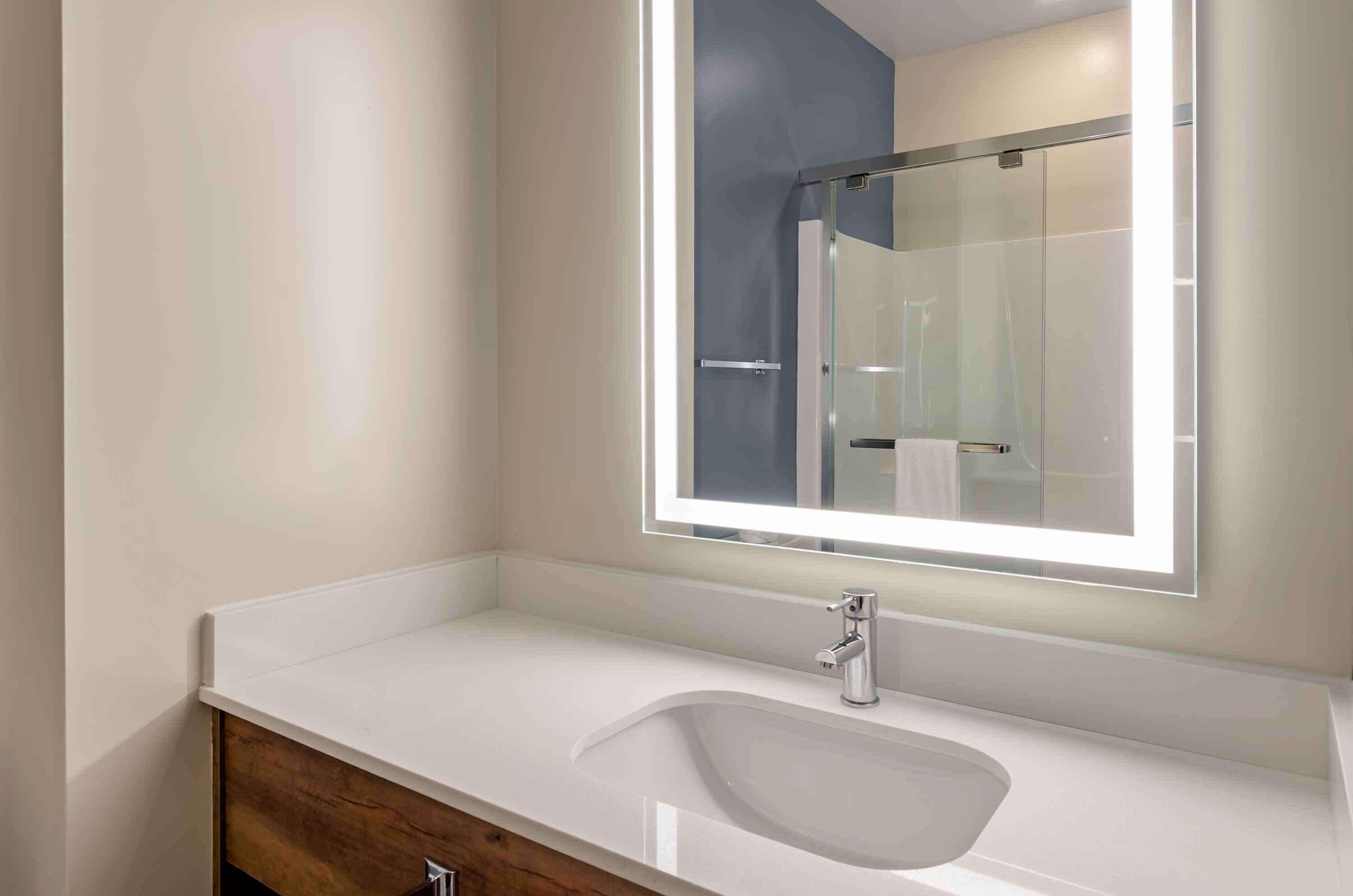 A modern bathroom with a white sink, a mirror with a light, and a glass shower enclosure.