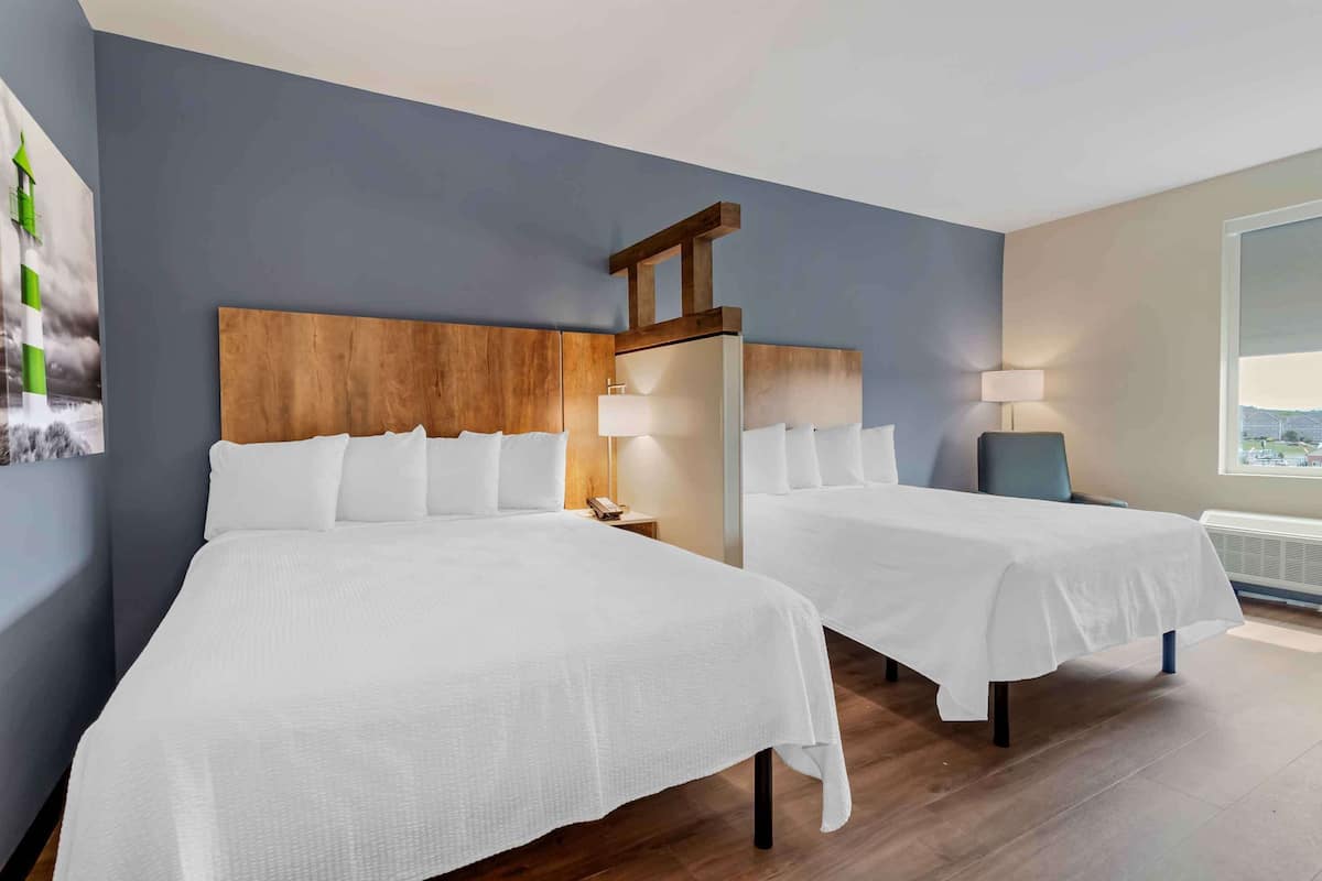 A hotel room with two beds, a wooden headboard, bedside lamps, and a large window with a view.