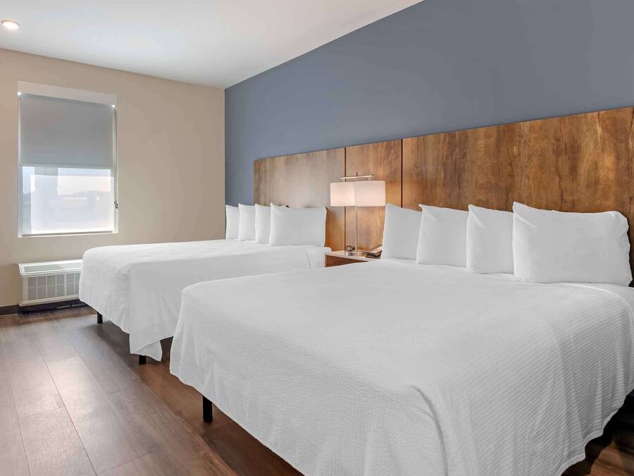A hotel room with two beds, a wooden headboard, a bedside lamp, and a window with blinds.