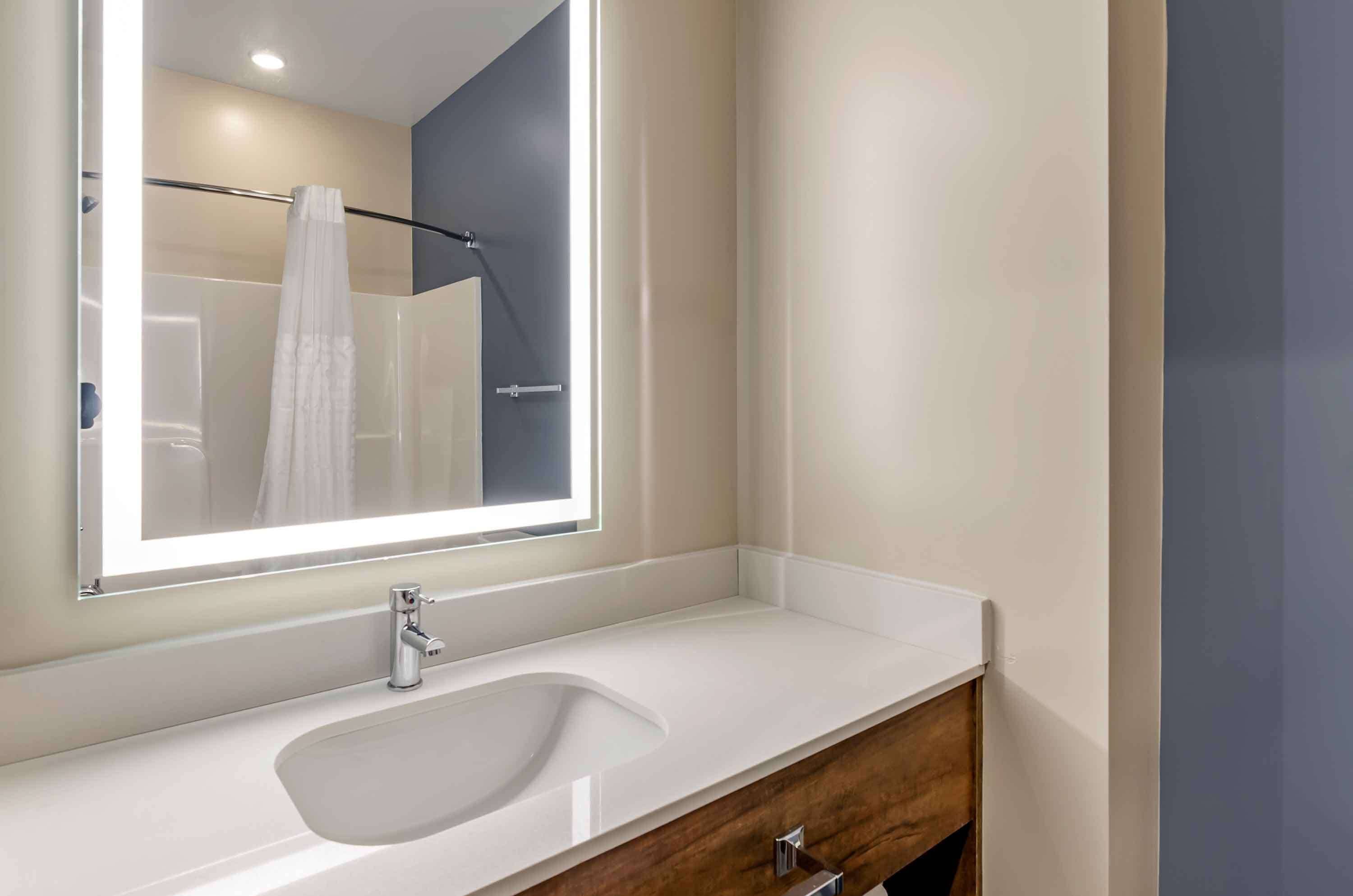 A modern bathroom with a large mirror, a white sink, and a wooden vanity.