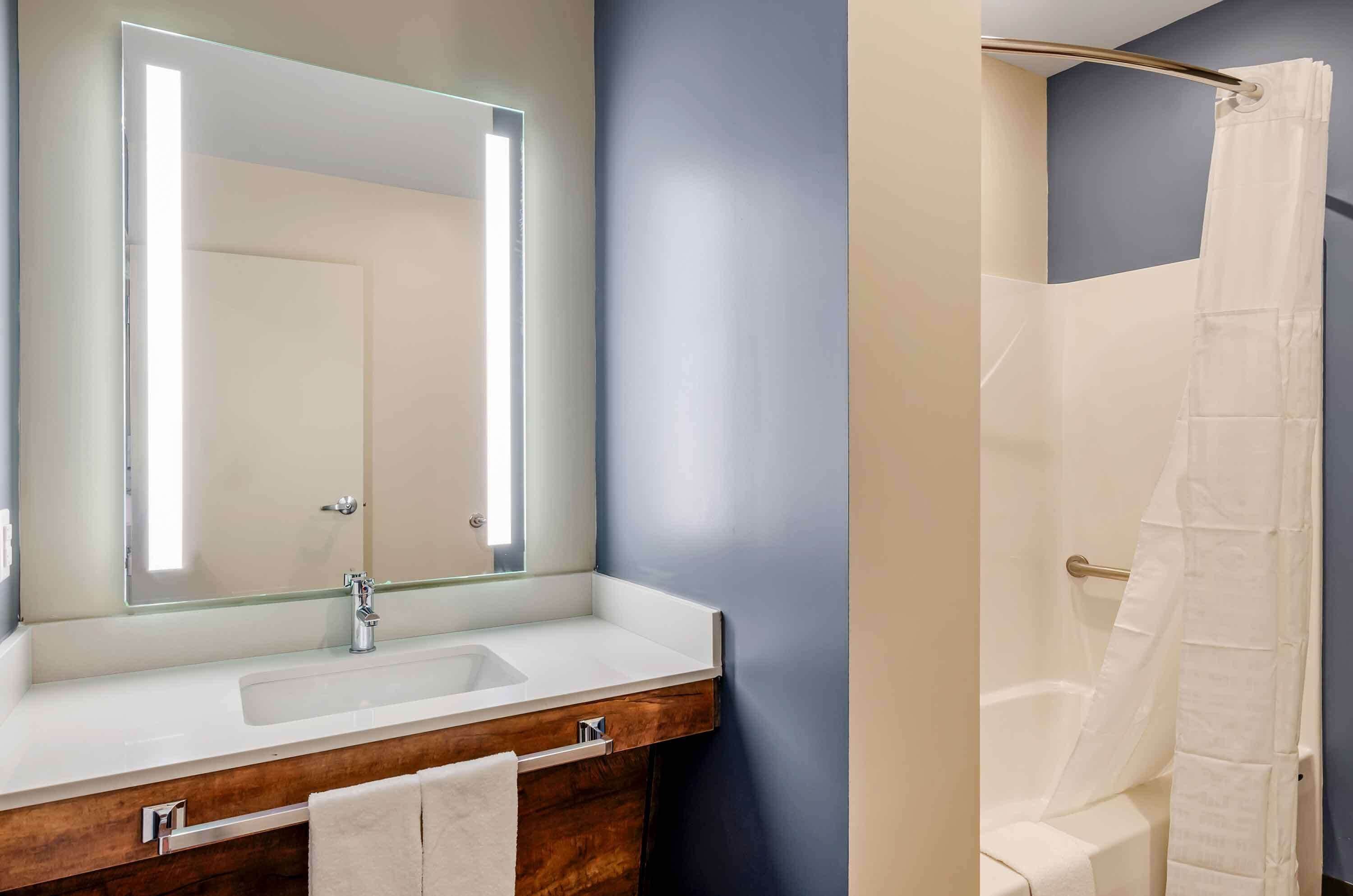 A bathroom with a large mirror, a sink, and a shower.
