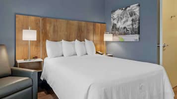 A hotel room with a large bed, two bedside tables, a chair, a painting on the wall, and a door.
