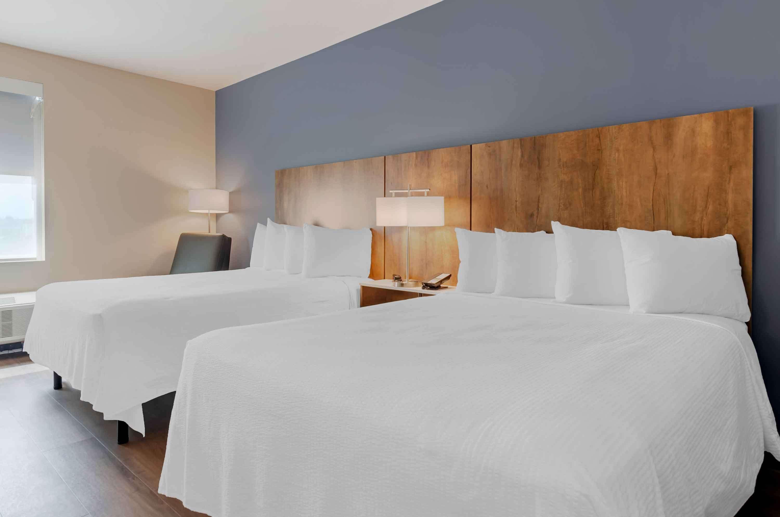 Habitación de hotel con dos camas, cabecero de madera, lámparas de noche y un ventanal grande.