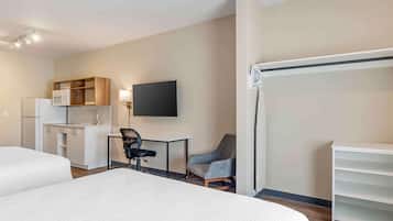 A hotel room with a bed, a desk with a chair, a television, a kitchenette, and a wardrobe.