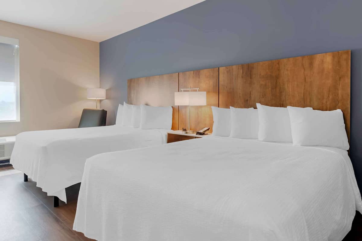 A hotel room with two beds, a wooden headboard, bedside lamps, and a large window.