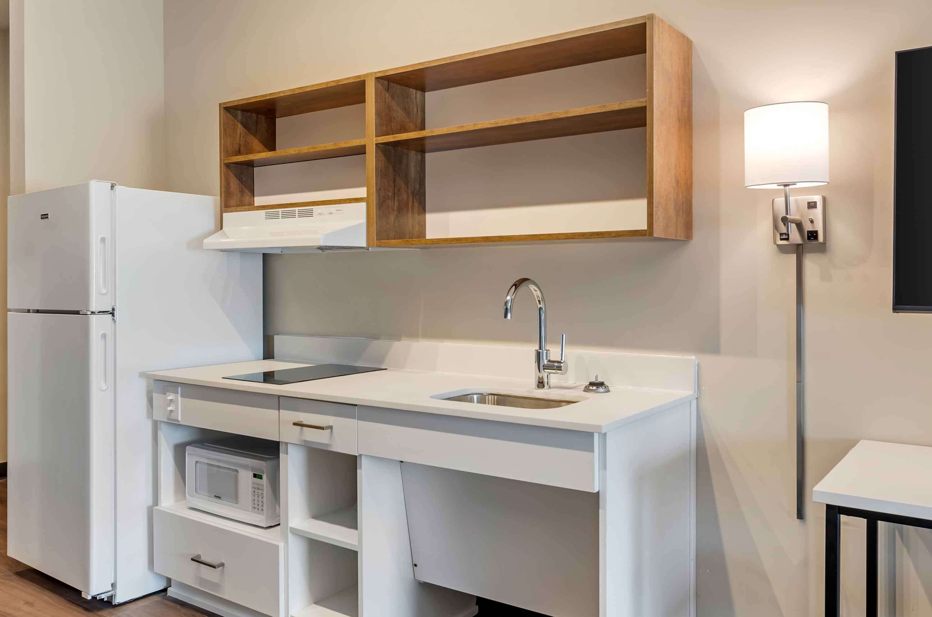 A compact kitchenette with a white refrigerator, microwave, and sink.