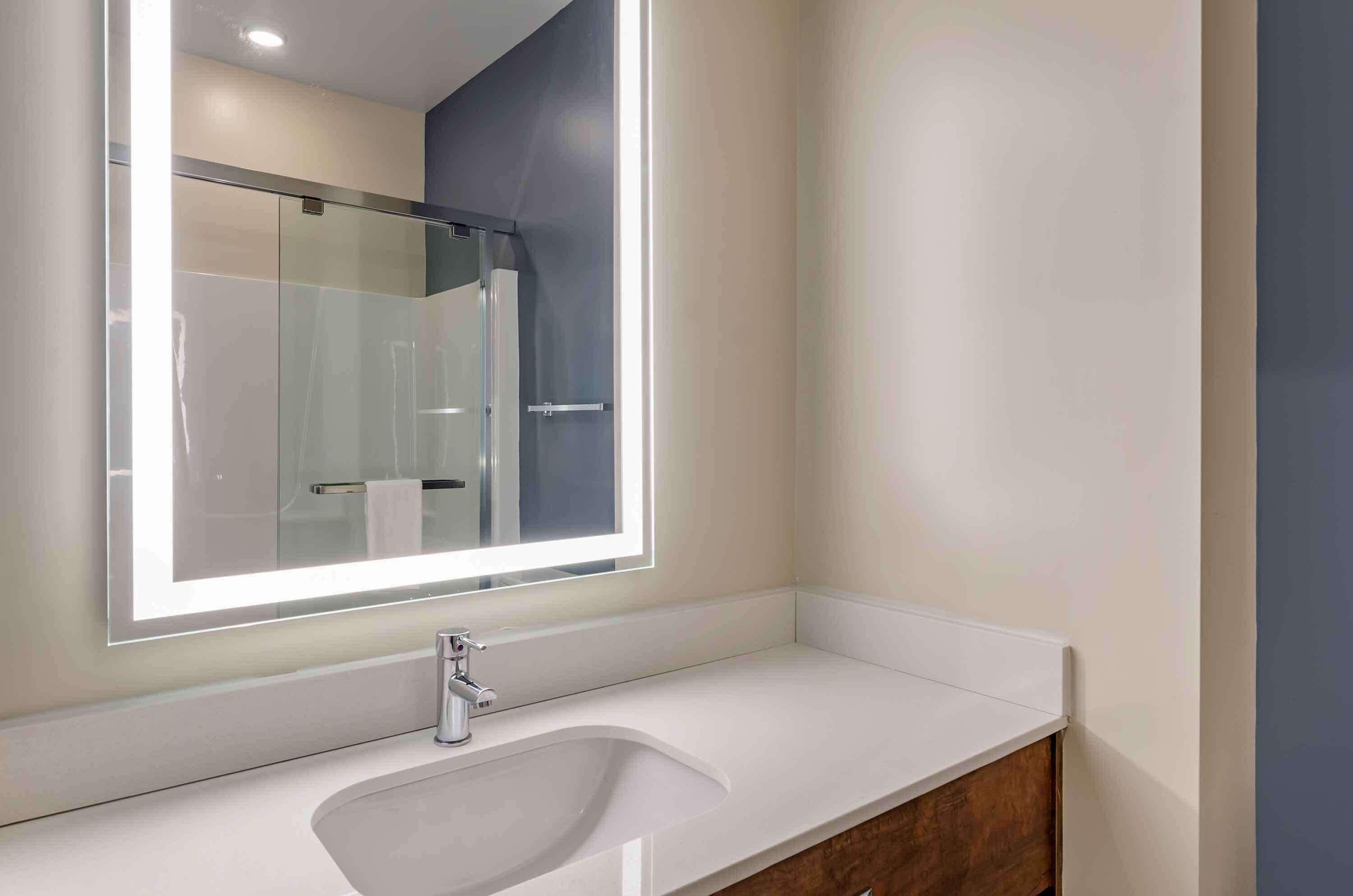 Une salle de bain moderne avec un grand miroir, un lavabo blanc et une douche à parois de verre.