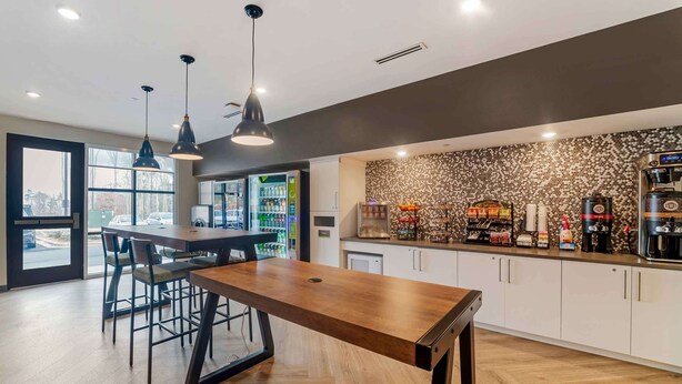 A modern kitchen with a wooden table, bar stools, pendant lights, and a coffee station. - Extended Stay America Premier Suites - Asheville (Asheville)