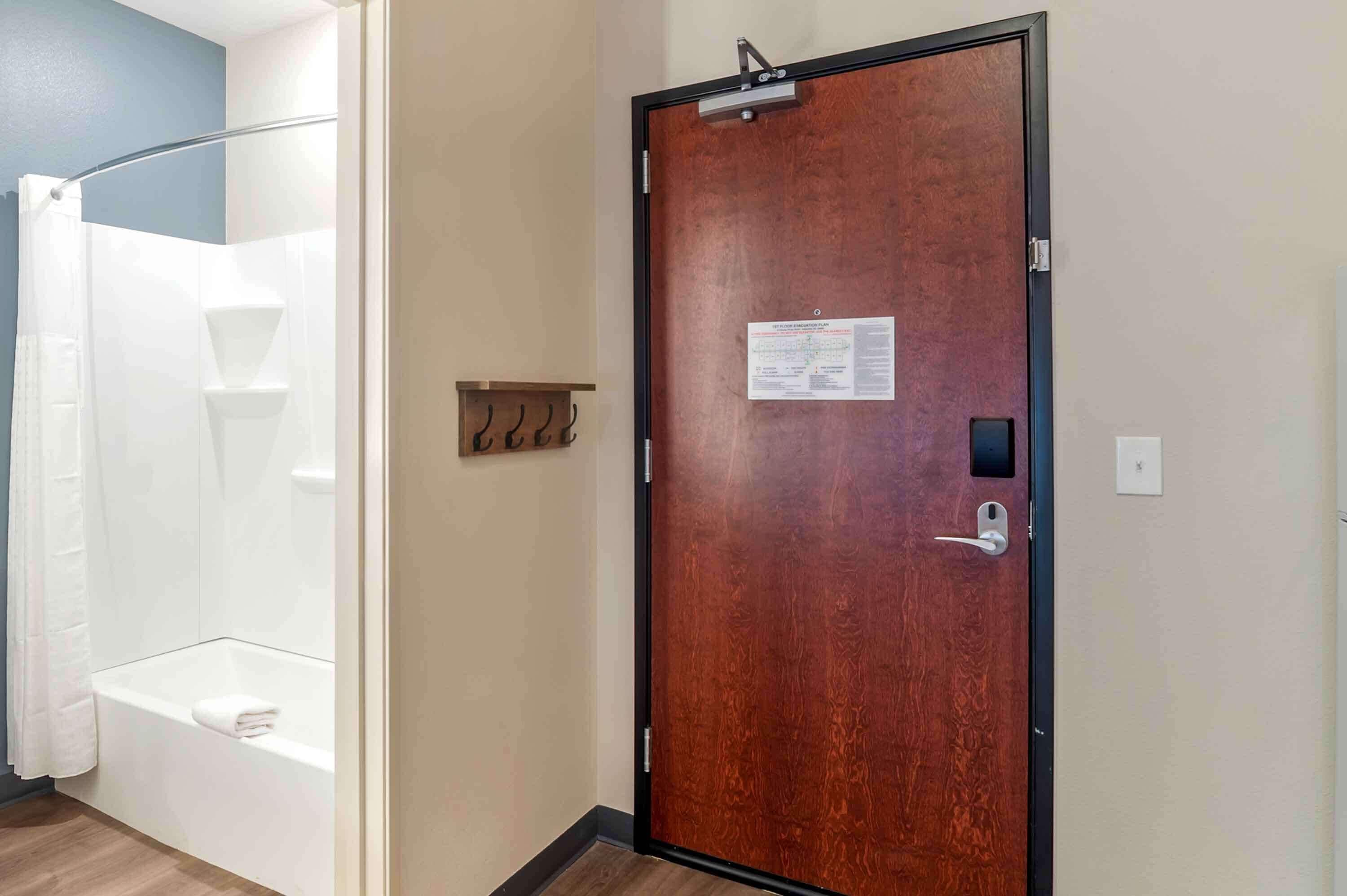 A hotel room with a wooden door, a shower, and a towel on the floor.