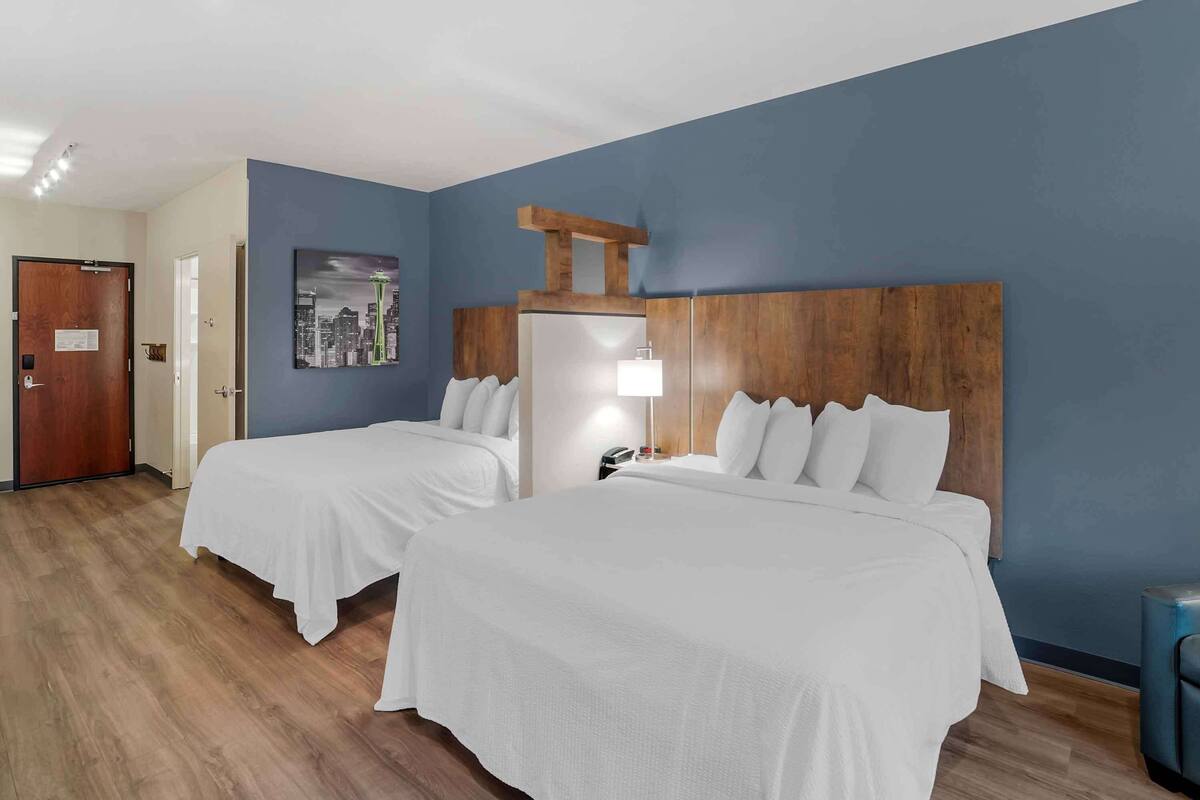 Una habitación de hotel con dos camas, un cabecero de madera, un cartel con un paisaje urbano y una puerta.