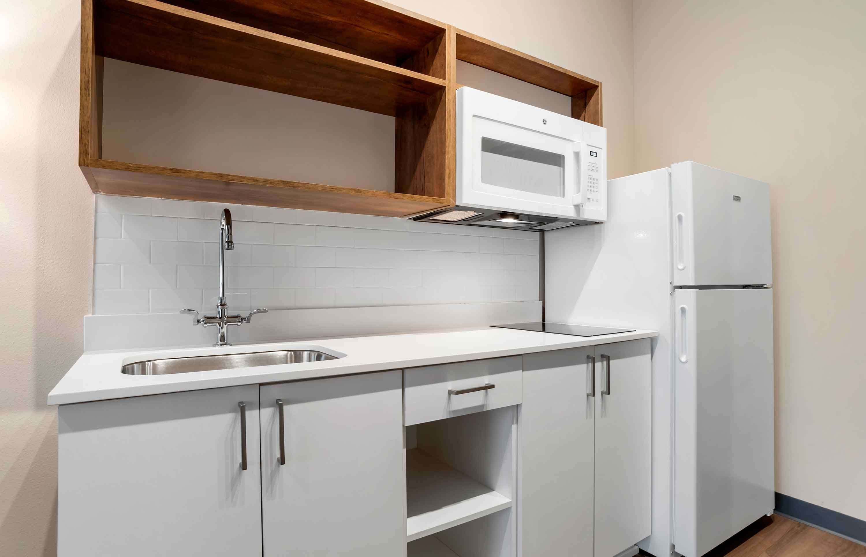 A compact kitchen with white cabinetry, a stainless steel sink, a microwave, and a refrigerator.