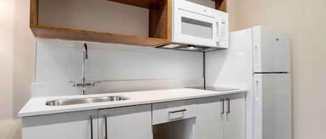 A compact kitchen with white cabinetry, a stainless steel sink, a microwave, and a refrigerator.