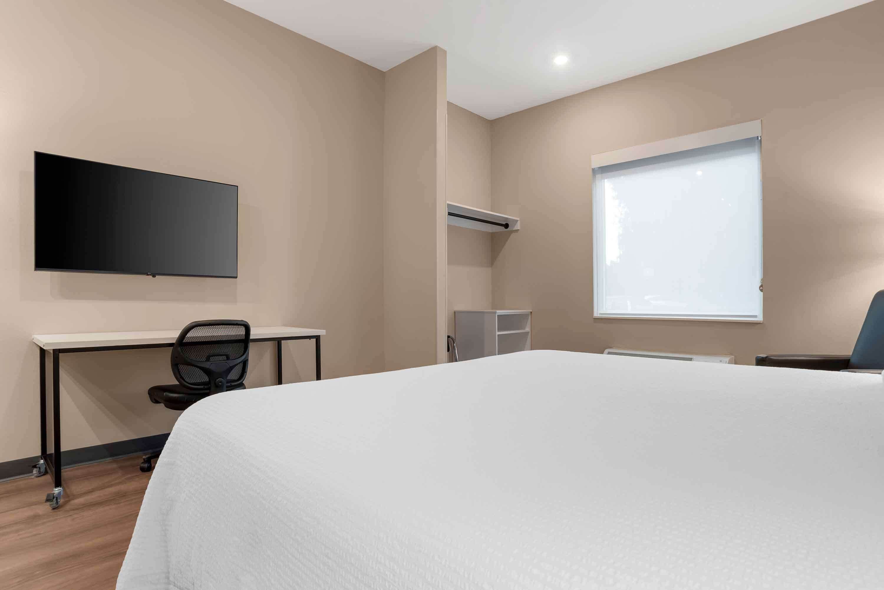 Habitación de hotel con cama, escritorio, silla, televisor de pantalla plana, ventana y aire acondicionado.