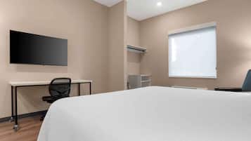 Habitación de hotel con cama, escritorio, silla, televisor de pantalla plana, ventana y aire acondicionado.