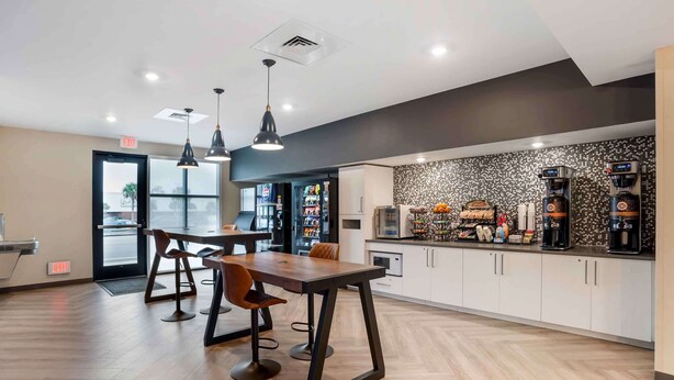 A modern kitchen with a coffee station, bar stools, and a large window.