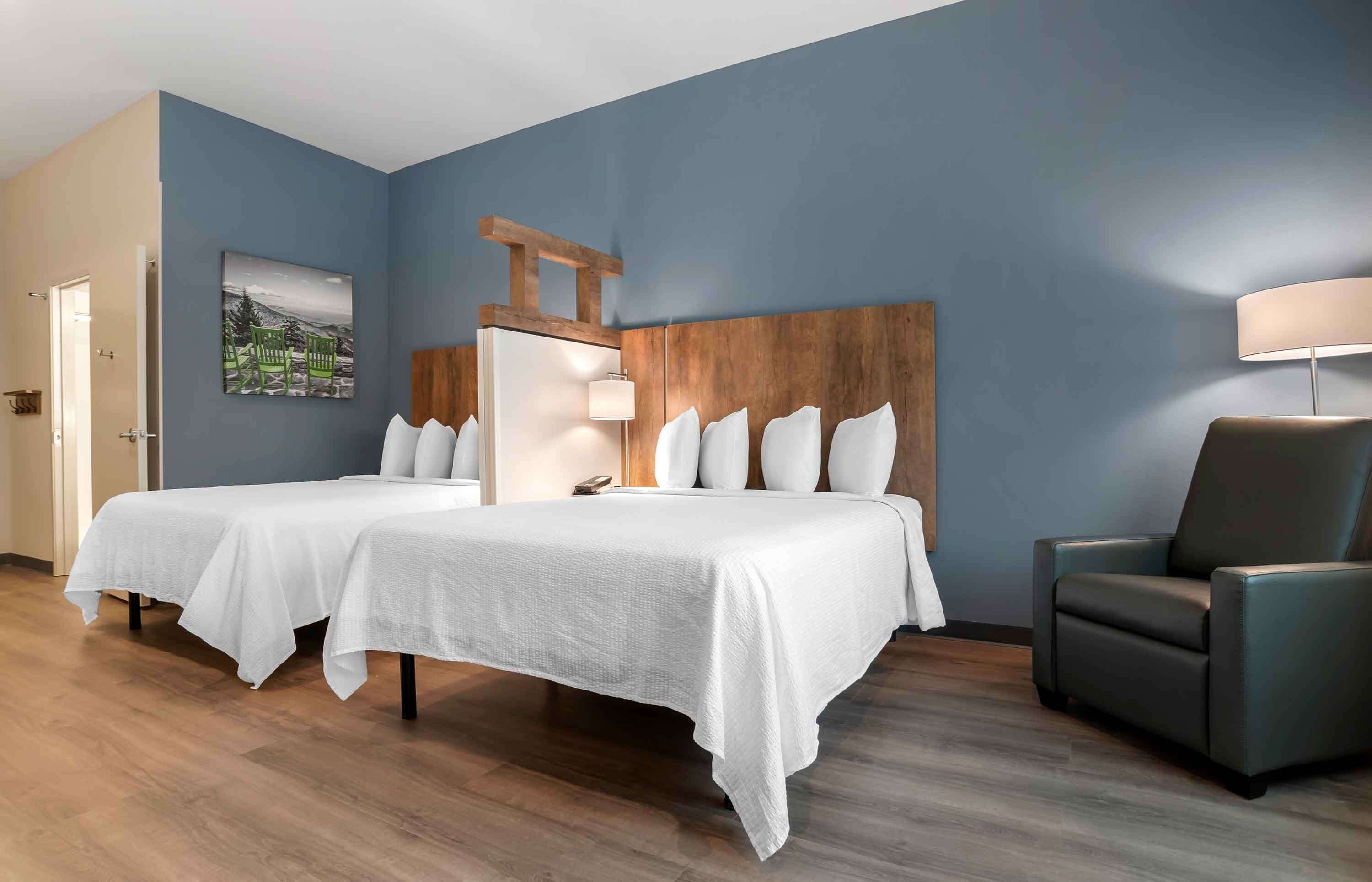 Una habitación de hotel con dos camas, un cabecero de madera, una lámpara y una silla.