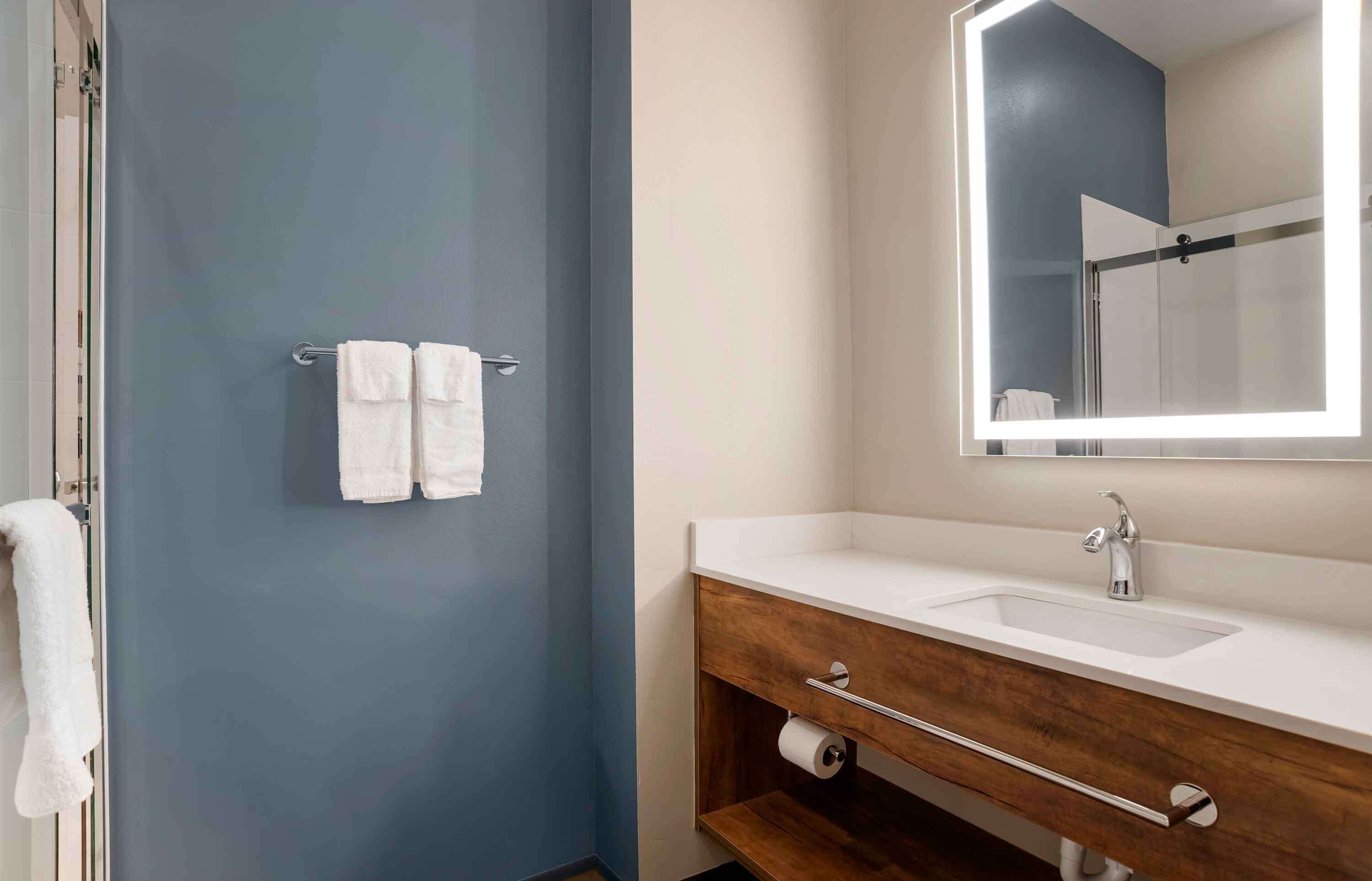 Un baño con pared azul, lavamanos blanco y espejo con marco iluminado.