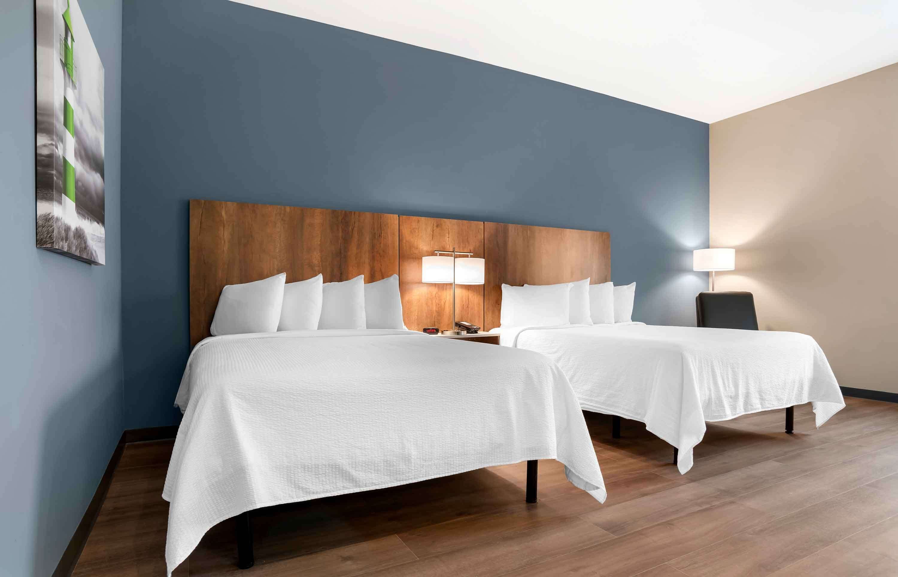 A hotel room with two beds, wooden headboard, white bedding, and a painting on the wall.