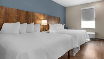 A hotel room with two beds, a wooden headboard, a bedside lamp, a window, and a wall-mounted air conditioner.