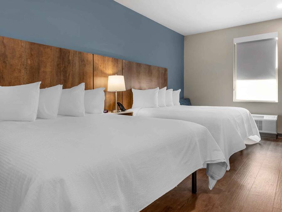 A hotel room with two beds, a wooden headboard, a bedside lamp, a window, and a wall-mounted air conditioner.